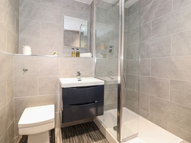 A bathroom with a toilet sink with a mirror and a glass shower enclosure at The Hayloft in Thirlmere