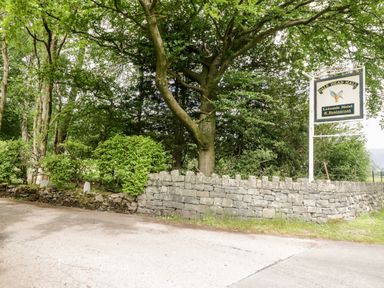 A stone wall along a road with trees and a sign for Dale Head Hall Lakeside Hotel and Restaurant at Thirlmere Suite in Thirlmere
