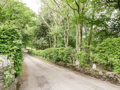 A narrow road bordered by stone walls and dense green trees at Thirlmere Suite in Thirlmere