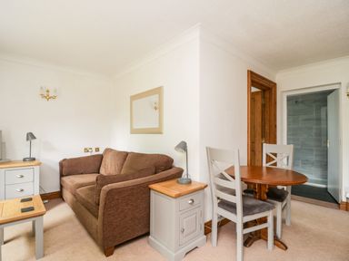 A small living room with a brown sofa a wooden table with two chairs a side table with a lamp and a mirror on the wall at Thirlmere Suite in Thirlmere