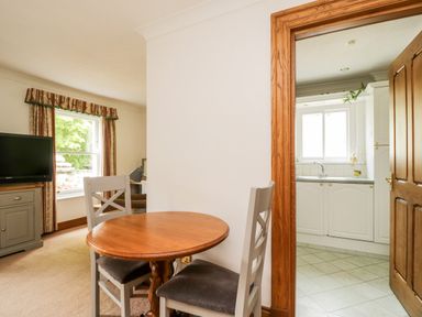 A dining area with a round wooden table and two chairs next to a kitchen with white cabinets at Thirlmere Suite in Thirlmere
