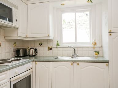 A kitchen with white cabinets a microwave toaster kettle sink and window at Thirlmere Suite in Thirlmere