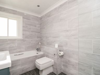 A bathroom with a bathtub a toilet a window and tiled walls at Thirlmere Suite in Thirlmere
