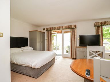 A bedroom with a bed a wardrobe a television on a cabinet and a round wooden table with chairs at Thirlmere Suite in Thirlmere