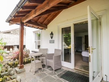 An outdoor patio with a wooden roof and two wicker chairs with a table outside a room at Thirlmere Suite in Thirlmere
