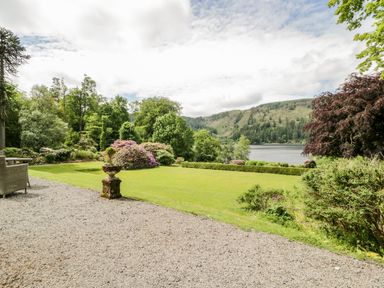 A garden with lawn shrubs and trees bordering a lake with hills in the background at Thirlmere Suite in Thirlmere