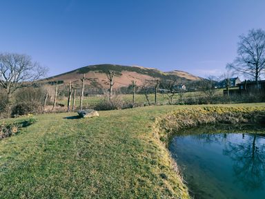 A grassy garden area with a pond and hills in the background at Scales Cottage Lorton near Cockermouth