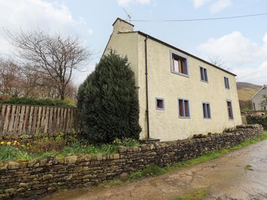 A stone wall and a house with multiple windows beside a dirt road at Scales Cottage in Lorton near Cockermouth