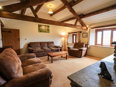 A living room with brown sofas wooden beams on ceiling a wooden coffee table and a statue of a dog on the fireplace at Scales Cottage in Lorton near Cockermouth