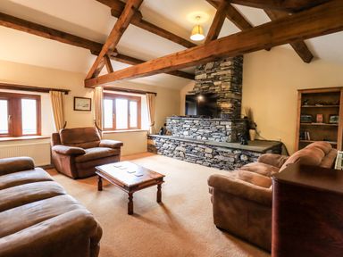 A living room with wooden beams stone fireplace brown sofas and a wooden coffee table at Scales Cottage in Lorton near Cockermouth