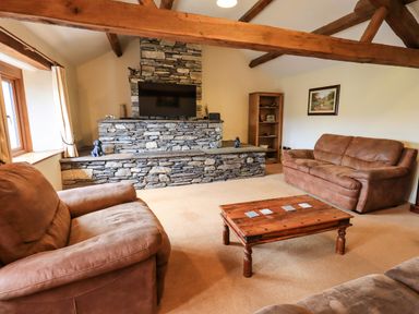 A living room with brown sofas a wooden coffee table and a stone fireplace at Scales Cottage in Lorton near Cockermouth