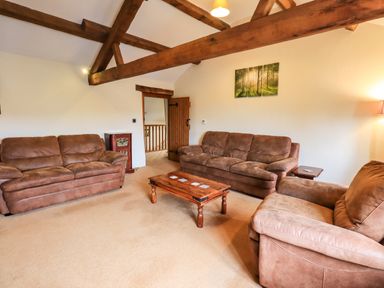 A living room with brown sofas wooden coffee table exposed beams and a wall painting at Scales Cottage in Lorton near Cockermouth