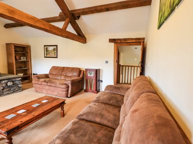 A living room with brown sofas a wooden coffee table wooden beams on ceiling and a bookshelf at Scales Cottage in Lorton near Cockermouth