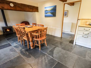 A dining room with a wooden table and chairs near a wood stove at Scales Cottage in Lorton near Cockermouth
