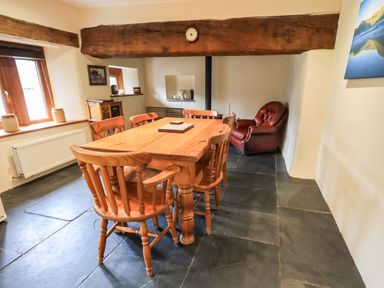 A dining room with a wooden table and chairs a red armchair and a window at Scales Cottage in Lorton near Cockermouth