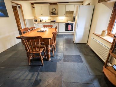 A kitchen with a wooden dining table and chairs a white refrigerator and cabinets at Scales Cottage in Lorton near Cockermouth