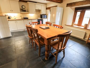 A kitchen with a wooden dining table and six chairs near a window at Scales Cottage in Lorton near Cockermouth