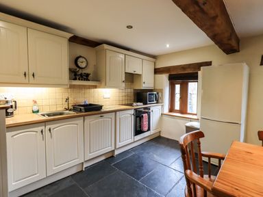 A kitchen with white cabinets a wooden table and chairs a white fridge and a small window at Scales Cottage in Lorton near Cockermouth