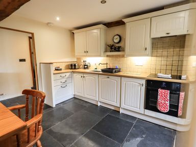 A kitchen with white cabinets black oven wooden table and chairs at Scales Cottage in Lorton near Cockermouth