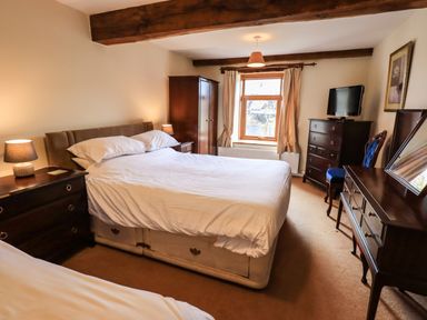 A bedroom with a double bed a wardrobe a chest of drawers a dressing table with mirror a chair and a window at Scales Cottage in Lorton near Cockermouth