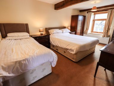 A bedroom with two beds two bedside tables lamps a wardrobe window and a wooden desk at Scales Cottage in Lorton near Cockermouth