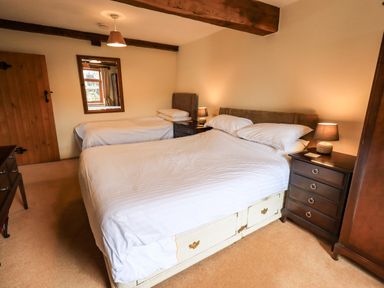 A bedroom with two beds wooden furniture and a mirror on the wall at Scales Cottage in Lorton near Cockermouth