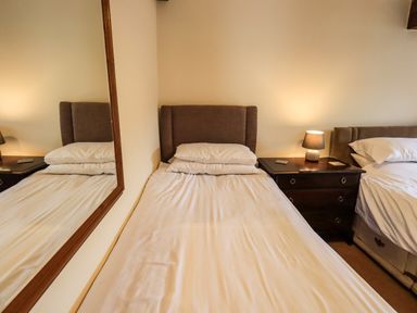 A bedroom with two beds a bedside table with a lamp and a large mirror on the wall at Scales Cottage in Lorton near Cockermouth
