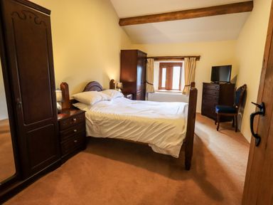 A bedroom with a bed table lamps wardrobe chest of drawers TV blue chair and a window at Scales Cottage in Lorton near Cockermouth