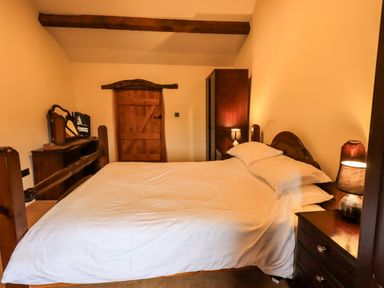 A bedroom with a wooden bed, bedside tables with lamps, a wardrobe, and a wooden door at Scales Cottage in Lorton near Cockermouth
