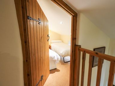 View through a wooden door into a small bedroom with two single beds and a wooden railing outside at Scales Cottage in Lorton near Cockermouth