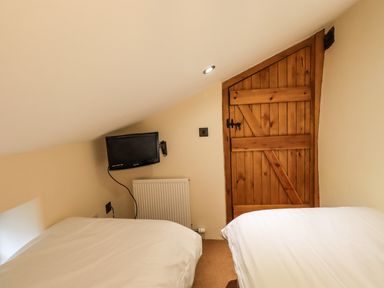 A small bedroom with two single beds a wooden door a wall-mounted television and a radiator at Scales Cottage in Lorton near Cockermouth