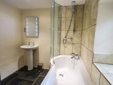 A bathroom with a bathtub with shower and a pedestal sink at Scales Cottage in Lorton near Cockermouth