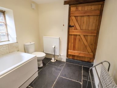 A bathroom with a bathtub a toilet a wooden door and a towel rack at Scales Cottage in Lorton near Cockermouth