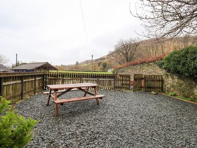 An outdoor area with a wooden picnic table surrounded by a wooden fence and stone wall at Scales Cottage in Lorton near Cockermouth