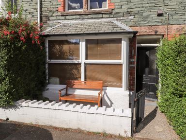 A small outdoor area with a wooden bench in front of a window and a black door with a gate at Archers in Keswick