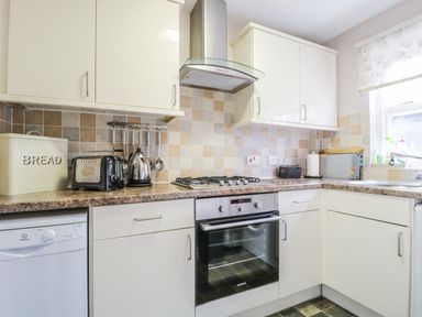 A kitchen with cream cabinets a tiled backsplash and countertop with appliances and a window at Swinside Cottage in Keswick