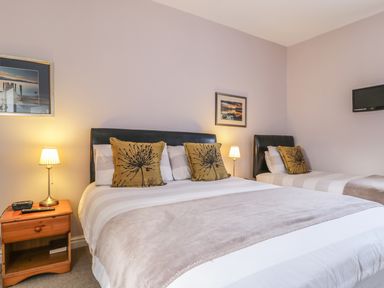 A bedroom with a double bed and a single bed two bedside tables with lamps and wall art at Swinside Cottage in Keswick