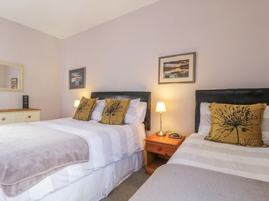 A bedroom with two beds a wooden nightstand lamp and pictures on the wall at Swinside Cottage Keswick