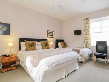 A bedroom with a double bed, a single bed, a wooden nightstand with a lamp, a black chair, and a window with floral curtains at Swinside Cottage in Keswick
