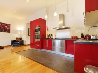 A kitchen with red cabinets stainless steel appliances and an armchair with a lamp in the corner at Keswick Loft in Keswick