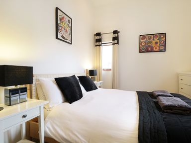 A bedroom with a double bed black and white bedding bedside tables with lamps curtains and framed artwork at Keswick Loft in Keswick