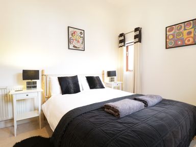 A bedroom with a bed with black and white bedding two nightstands with lamps and abstract paintings on the walls at Keswick Loft in Keswick