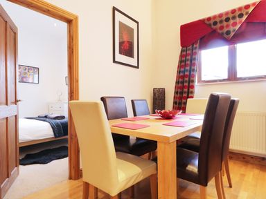 A dining room with a wooden table and mixed color chairs next to a window with patterned curtains at Keswick Loft in Keswick