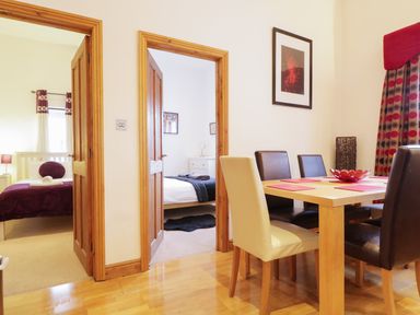 A dining area with a wooden table and four chairs near two doorways leading to bedrooms at Keswick Loft in Keswick