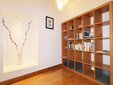 A wooden bookshelf with books and board games next to a white wall with a recessed shelf holding a white vase with two branches at Keswick Loft in Keswick
