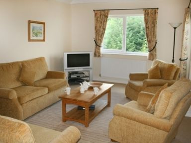 A living room with upholstered armchairs and a sofa around a wooden coffee table with tea set and a television at Whitbarrow Holiday Village Troutbeck 5 Ullswater