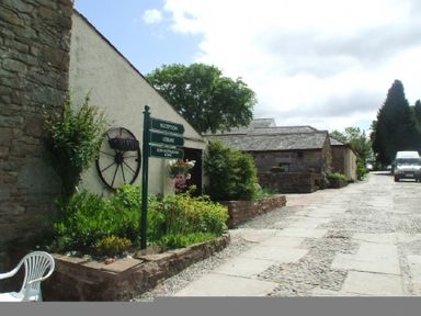 A stone-paved courtyard with garden beds and a signpost near stone buildings at Whitbarrow Holiday Village Troutbeck 5 Ullswater