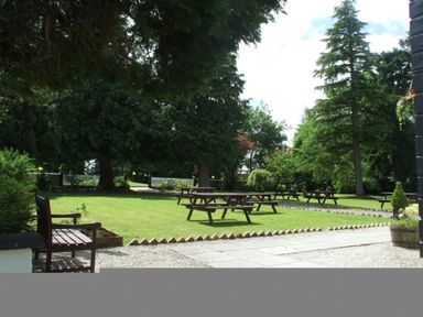 An outdoor garden area with picnic tables on grass and trees surrounding the space at Whitbarrow Holiday Village Troutbeck 5 Ullswater