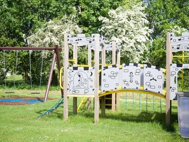 A playground with swings slide and climbing equipment on grass with trees in the background at Whitbarrow Holiday Village Troutbeck 5 Ullswater