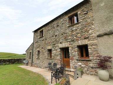 Stone house exterior with wooden windows and door patio furniture and planter on grass at Grayrigg Foot Stable in Grayrigg